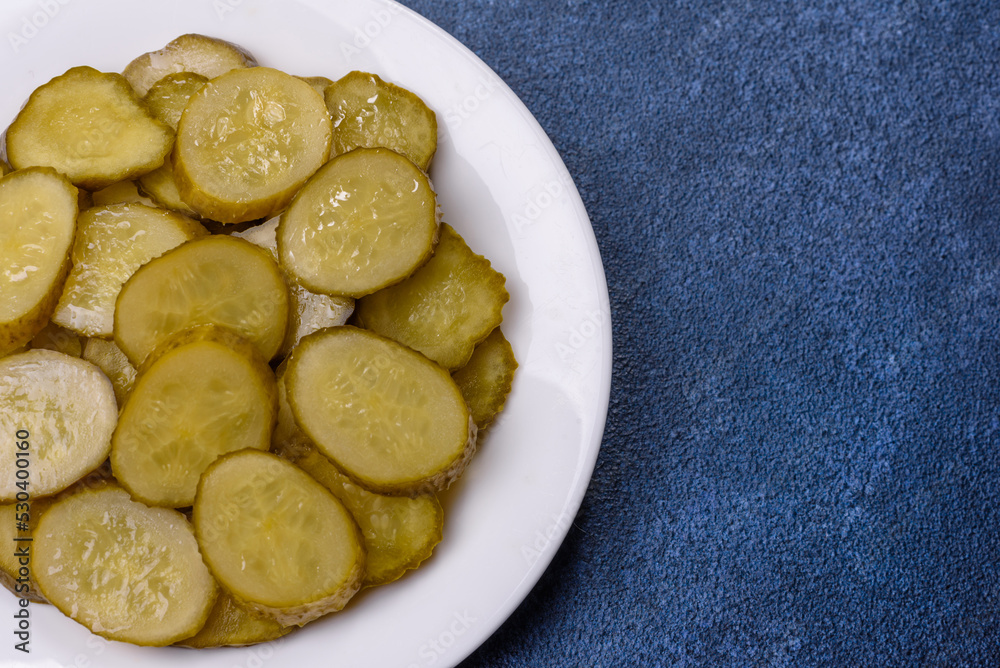Delicious salted, canned cucumbers cut into slices on a white ceramic plate
