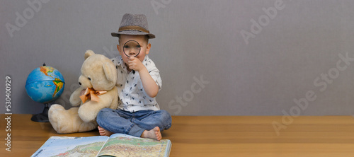 The boy is holding a bear and looking through a magnifying glass. A little boy studies the map of the world and learns lessons at school. Back to school. Education concept. High quality photo