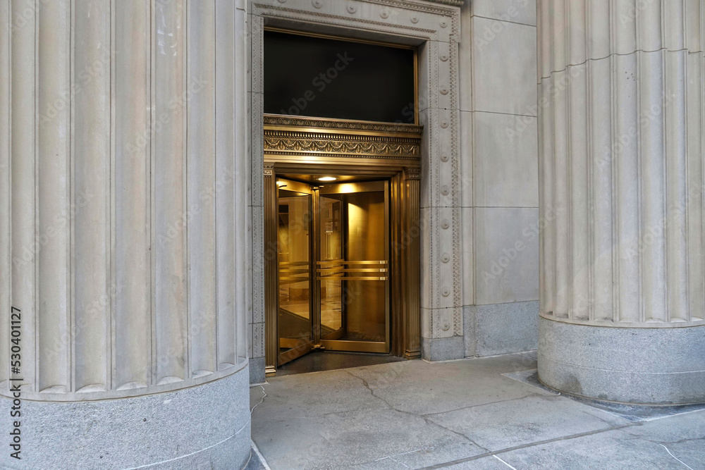 Building entrance, with brass revolving door in between large stone columns