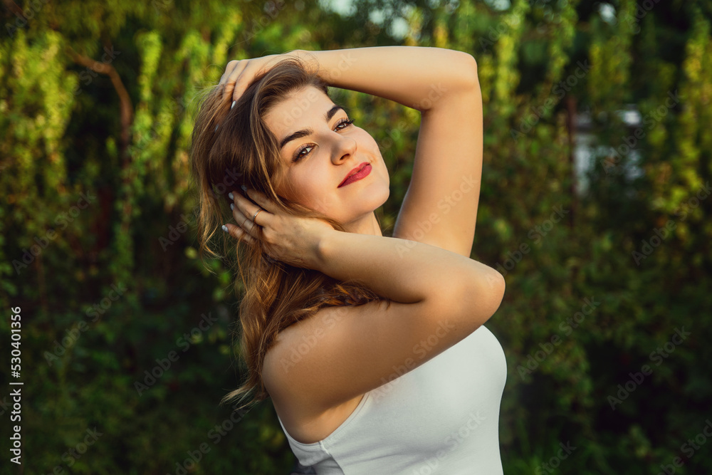 Young woman touches her hair in the garden at sunset .in a white shirt Young woman touches her hair in the garden at sunset .in a white shirt
