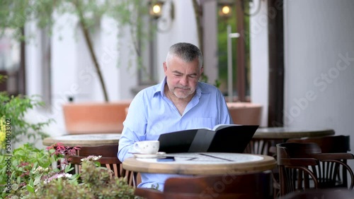 Handsome caucasian middle aged man hoosing lunch menu in street cafe.	