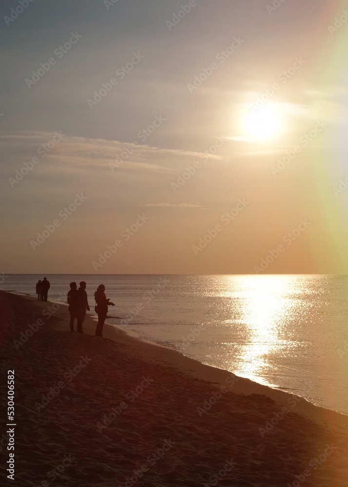 Sunset over the Baltic Sea. The Curonian Spit near Kaliningrad. People walk along the beach and admire the views Sunset over the Baltic Sea. The Curonian Spit near Kaliningrad. People walk along the beach and admire the views