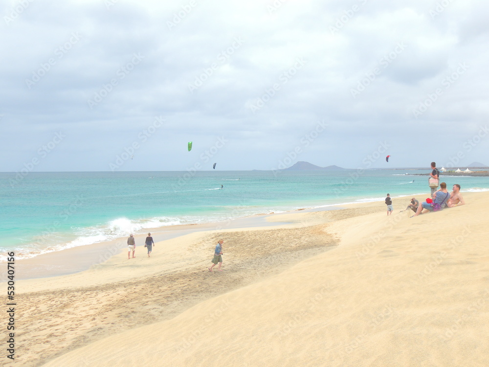 picture of the most famous beach for kitesurf in santa maria, sal island, cape verde. white sand, green and blue sea. people walking on the beach. postcard effect . windy. cloudy. sand dune.