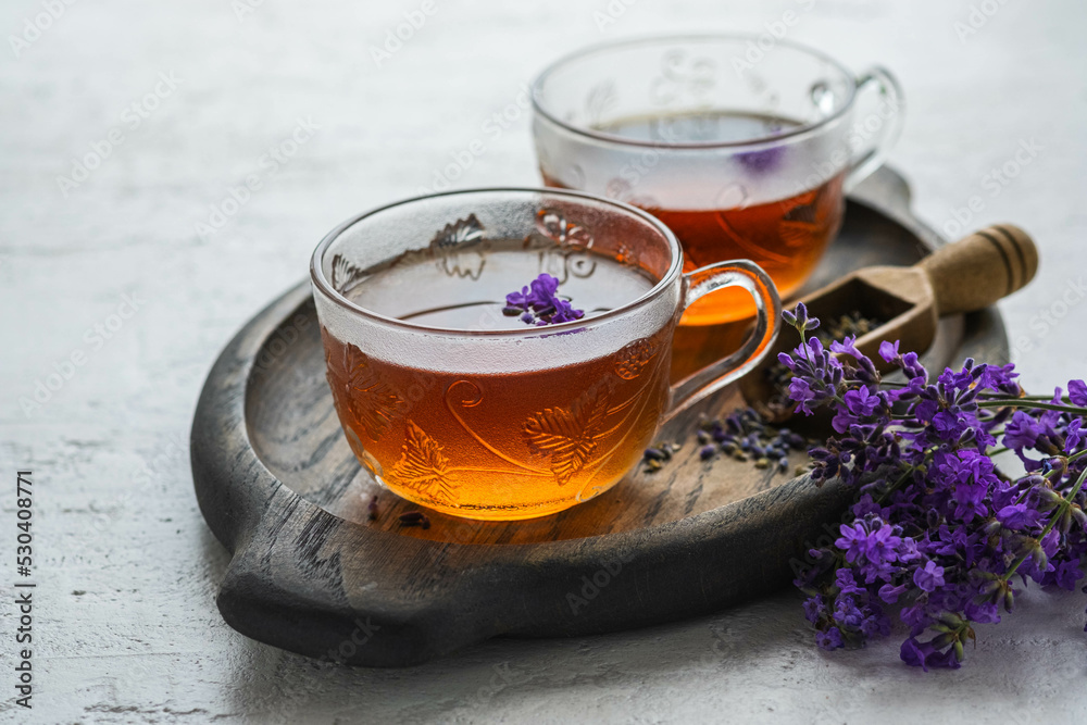 Lavender tea in transparent glass cups on a wooden tray on a light concrete background. Hot drinks. Lavender tea in transparent glass cups on a wooden tray on a light concrete background. Hot drinks.