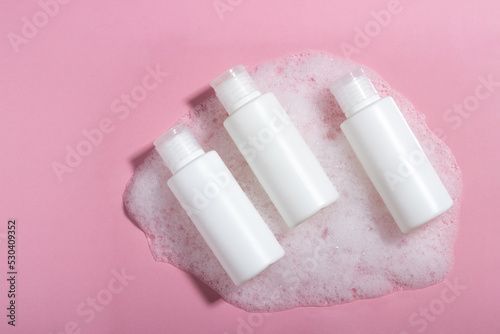 Cosmetics for face, body and hair care. Moisturizer, shampoo or facial cleanser on pink background with foam
