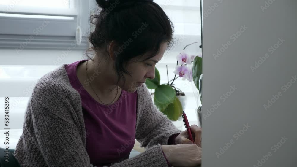 Young Woman Writing Checklist Note. Housewife Sitting at Desk Table Near Window in Apartment. 2x Slow motion 60fps 4K