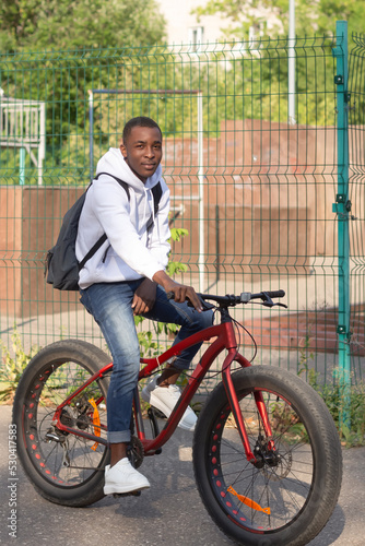 A happy African American man rides a bicycle through a public park. Portrait. Sports and recreation
