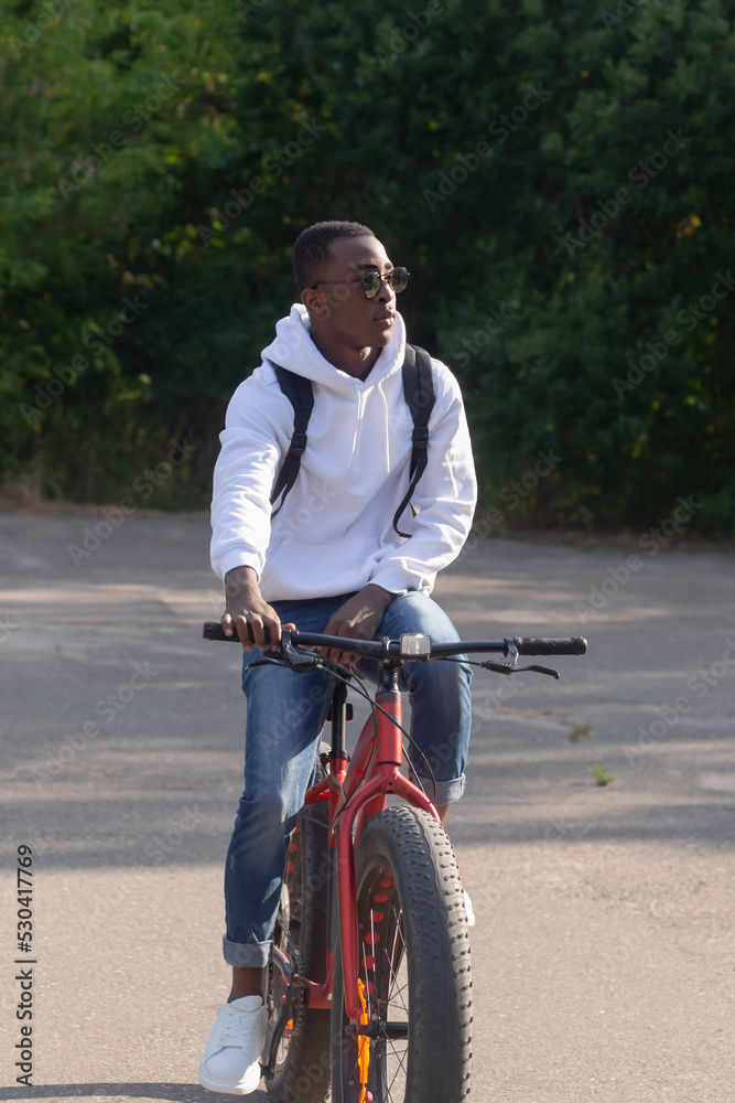 Obraz premium A happy African American man rides a bicycle through a public park. Portrait. Sports and recreation