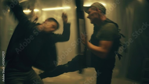 Male criminal or bandit and policeman having aggressive close fight in dim underground room illuminated by LED lamps. Action or criminal movie scene