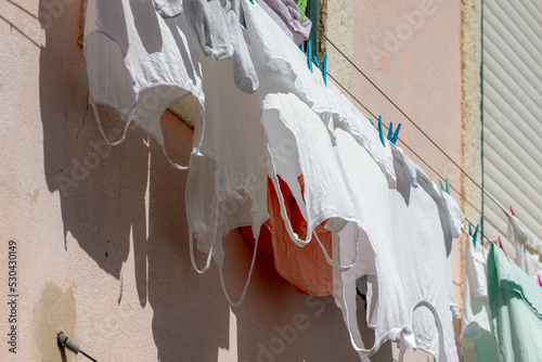 Hanging clothes on the clothesline outside building, Typical Portuguese style drying laundry under the sun in summer, White t-shirt on the washing line in city with cement wall as background, Portugal