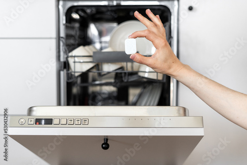 Person holding capsule in front of dishwasher machine
