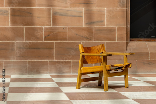 Sling chair. Empty modern leather and wood seat alone in waiting area. Minimalist space interior design.