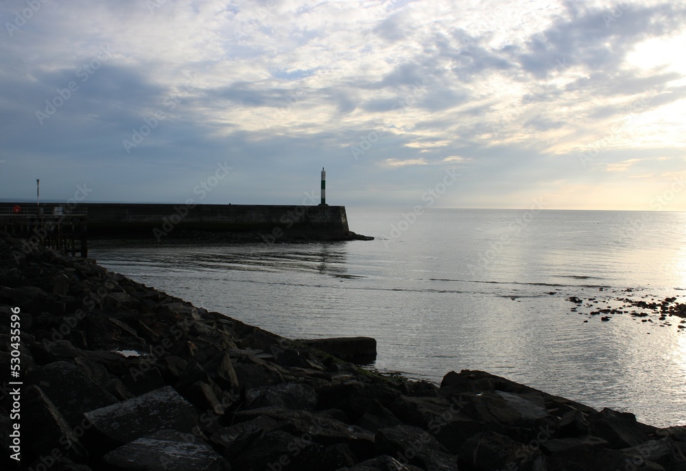Lighthouse at Aberystwyth with an atmospheric sky with the sun reflecting off the sea