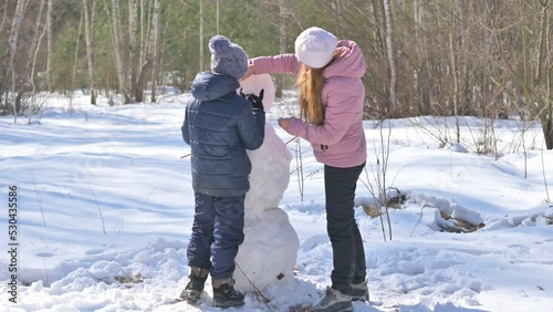 Winter fun. Happy mom and son are building a snowman in a snowy park. Lovely family at winter holidays.