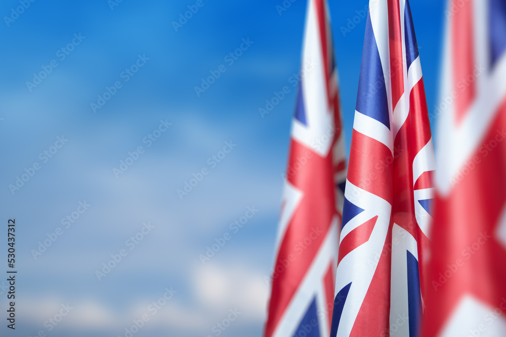 National flags of United Kingdom on a flagpole on blue sky background. Lowered UK flags. Background with place for your text.