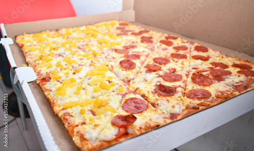 Pizza rectangular de pepperoni con hawaiana en su caja 
