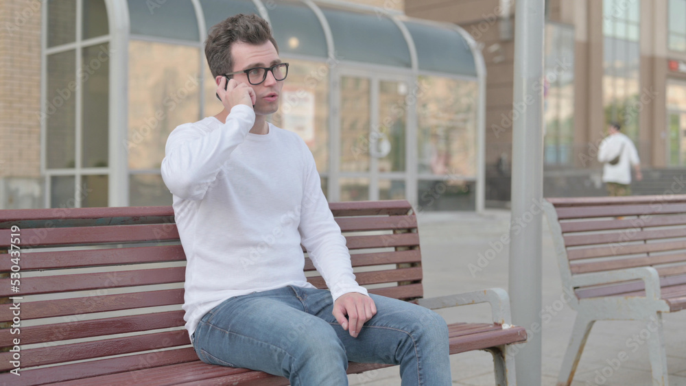 Young Man Talking on Phone while Sitting Outdoor on Bench