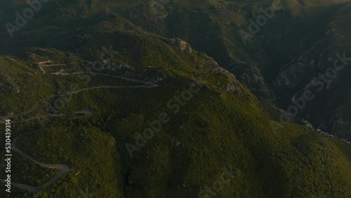 Drone pans trough beautiful green hills revealing a town and sunrise at the end, curvy road crosses the hills, Filmed in. Margalla Hills, Islamabad