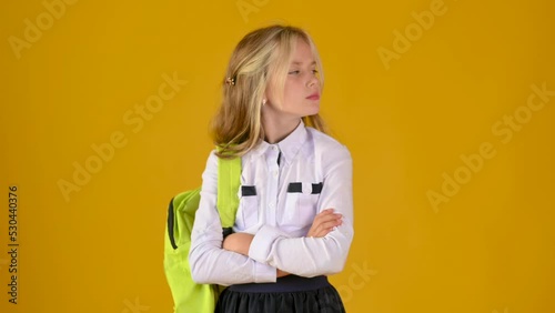 Close up portrait of a schoolgirl with a briefcase is offended and angry on a studio yellow background.	 photo