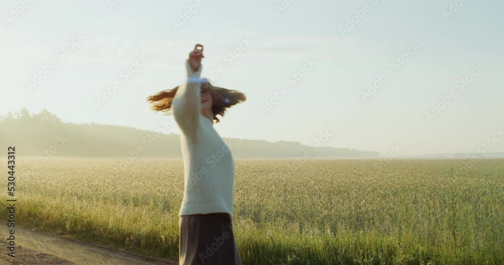 A beautiful young red-haired woman laughs as she dances and whirls on a gravel road near an agricultural field, enjoying the warm rays of the rising sun. 4k, video, red komodo A beautiful young red-haired woman laughs as she dances and whirls on a gravel road near an agricultural field, enjoying the warm rays of the rising sun. 4k, video, red komodo