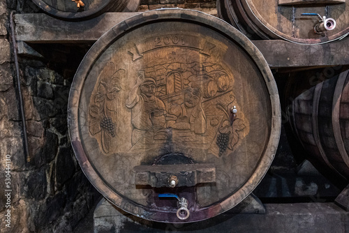 Wooden wine barrel with the motif of grapes, a waiter and a visitor behind the bar. Bela Krajina, Slovenija