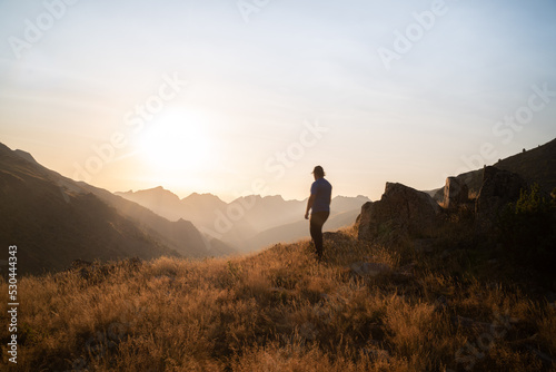 man standing on a mountain summit looking to the red sunset