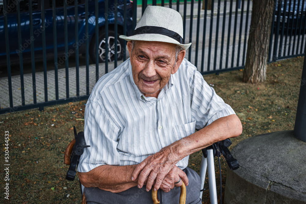 Abuelo sentado en su andador observando relajado el parque disfrutando del  día con una sonrisa en la cara con su sombrero, su bastón y su andador foto  de Stock | Adobe Stock