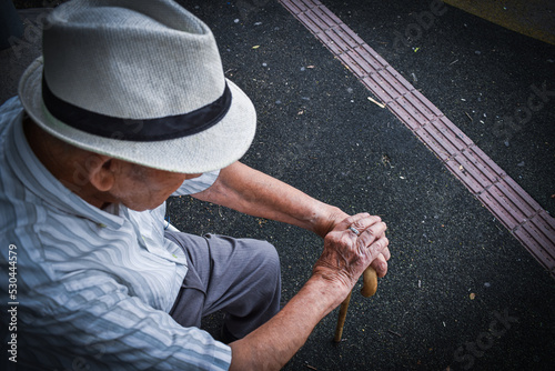 Abuelo anciano sentado con sus manos sobre su bastón y con su sombrero 