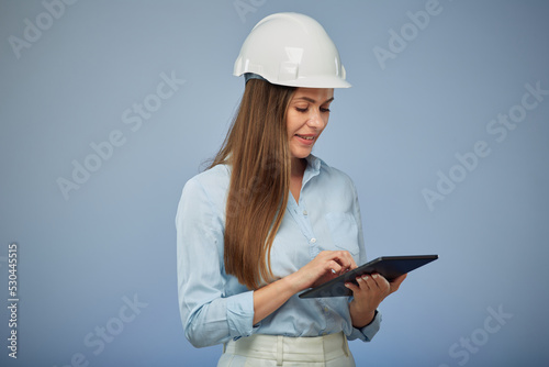 Smiling woman architect or engineer in safety industrial helmet using tablet. Isolated female portrait.