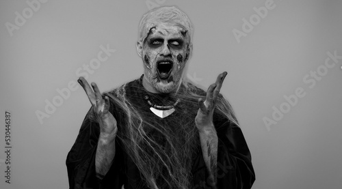 Dissatisfied frightening man with Halloween zombie bloody wounded makeup asking reason of failure, expressing disbelief irritation, feeling bored, disappointed in result, bad news. Sinister undead guy