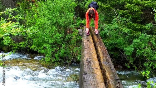 Young woman hiker, hiking walking across strong stream current creek, crossing river in forest on conundrum hot springs trail, Colorado with wet slippery log wood bridge in wilderness photo