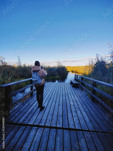 Young woman standing on a wooden pier and taking photo of a large crayfish lake. State Natural Reserve Cancer Lakes , St. Petersburg