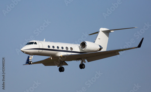 Fotografia Modern comfortable private jet flying in blue sky, approaching landing