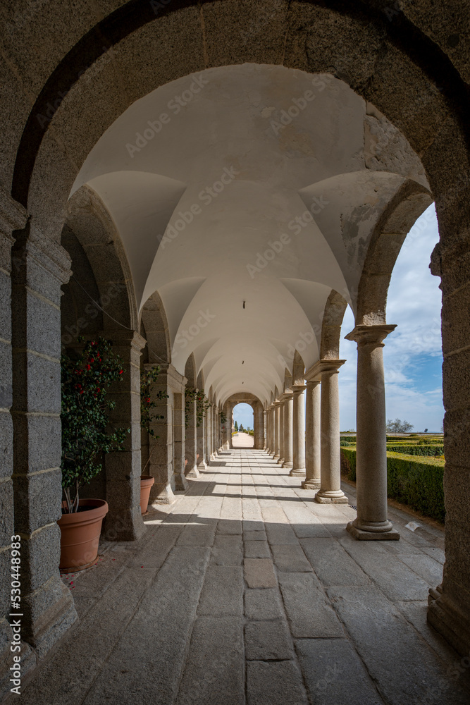 arched walkway with granite floors and gardens with hedges on the open side