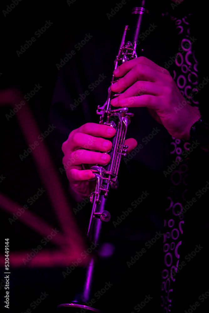 Fototapeta premium A musician with a clarinet next to a music stand illuminated with purple light