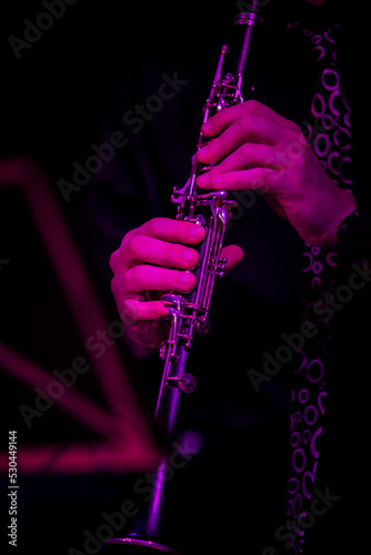 A musician with a clarinet next to a music stand illuminated with purple light