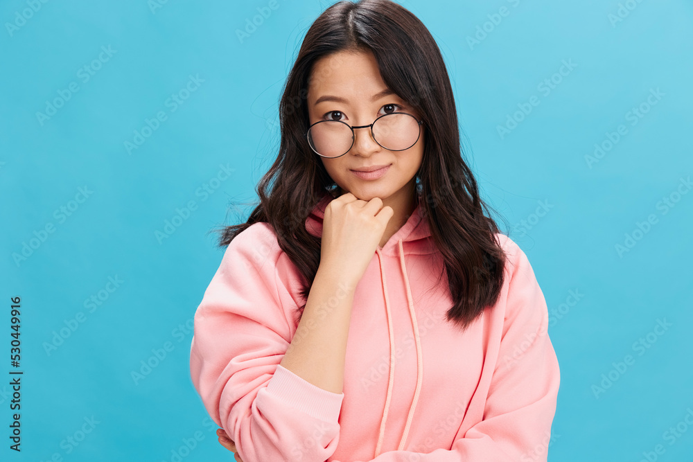 Cutie Asian student young lady in pink hoodie sweatshirt wear round glasses smiles at camera posing isolated on blue studio background. The best offer for ad. Eyewear for vision correction concept Cutie Asian student young lady in pink hoodie sweatshirt wear round glasses smiles at camera posing isolated on blue studio background. The best offer for ad. Eyewear for vision correction concept