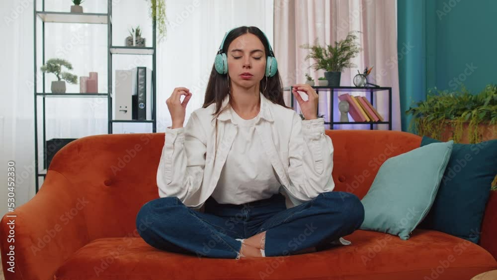 Keep calm down, relax, inner balance. Adult girl breathes deeply with mudra gesture, eyes closed meditating with concentrated thoughts, peaceful mind. Young woman sit at home in living room on couch Keep calm down, relax, inner balance. Adult girl breathes deeply with mudra gesture, eyes closed meditating with concentrated thoughts, peaceful mind. Young woman sit at home in living room on couch