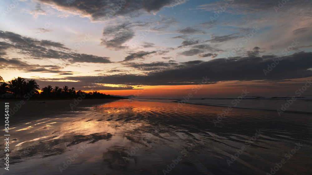 Vivid dawn colors at a tropical beach and sky clouds reflection on wet sand, shown in Chiriqui, Panama.