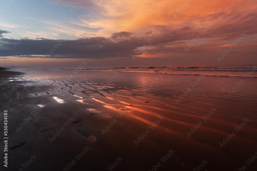 Vivid dawn colors at a tropical beach and sky clouds reflection on wet sand, shown in Chiriqui, Panama.