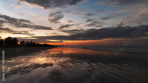 Vivid dawn colors at a tropical beach and sky clouds reflection on wet sand, shown in Chiriqui, Panama.