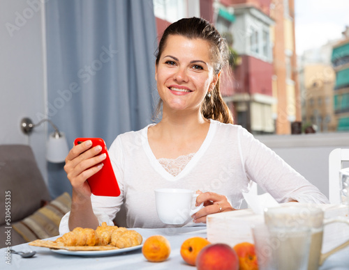 Portrait of young woman using phone at table with tea and peaches