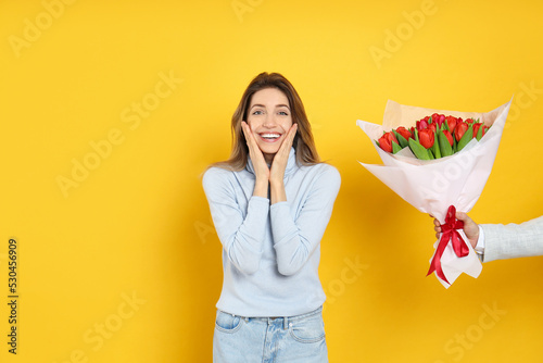 Happy woman receiving red tulip bouquet from man on yellow background. 8th of March celebration #530456909