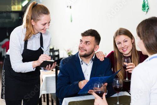 Woman waiter is taking order from clients in restaurante indoor.