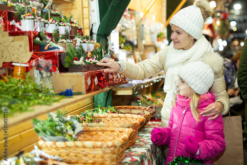 Young girl and her mother are buying Christmas ornamentals in the market outdoor. High quality photo