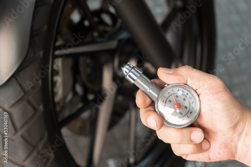 Man holding pressure gauge for checking  motocycle tyre pressure ,maintenance,repair motorcycle concept in garage .selective focus
