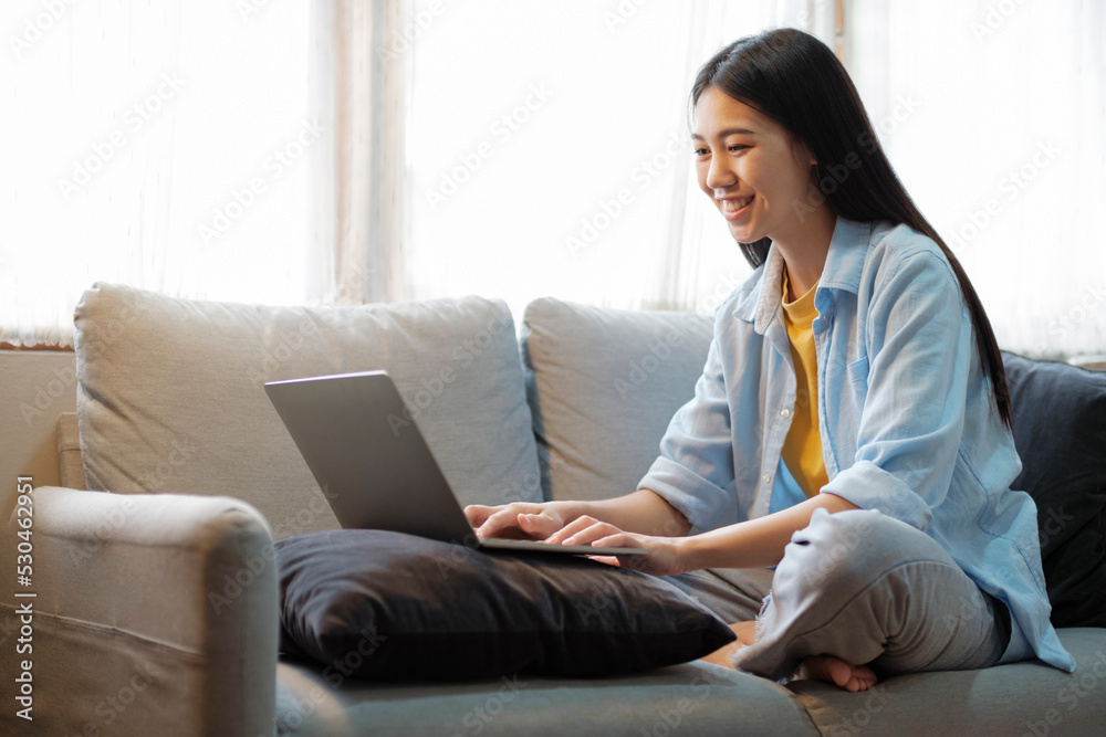 Young asian woman smiling and using laptop while sitting on couch at home. Young asian woman smiling and using laptop while sitting on couch at home.