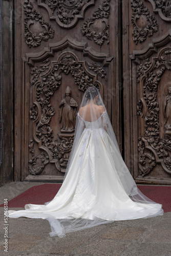 Bride wearing white wedding dress at the entrance of old church.
