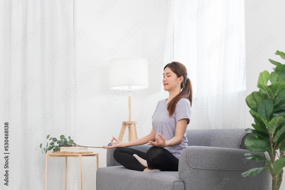 Yoga exercise concept, Young Asian woman doing yoga exercise in lotus pose on couch in living room Yoga exercise concept, Young Asian woman doing yoga exercise in lotus pose on couch in living room