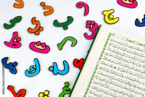 Colorful Arabic letters and kitab Al-Quran on white background photo